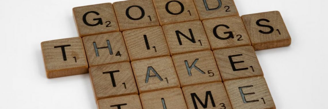Close-up of wooden tiles spelling 'Good Things Take Time' on a white background.
